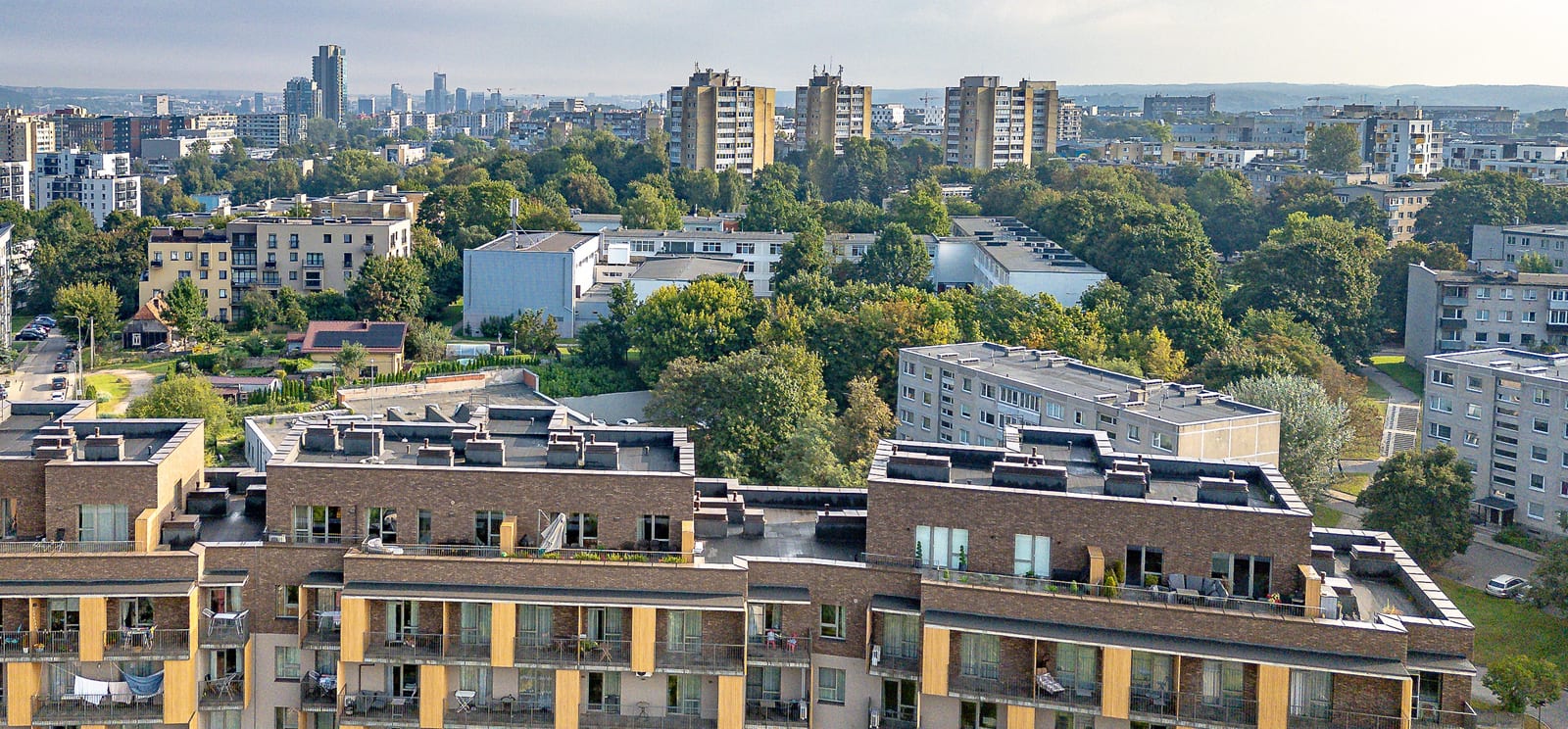 Vilnius seen from roof level: the trees of the district, the apartment houses around it and the business-centre towers on the horizon.